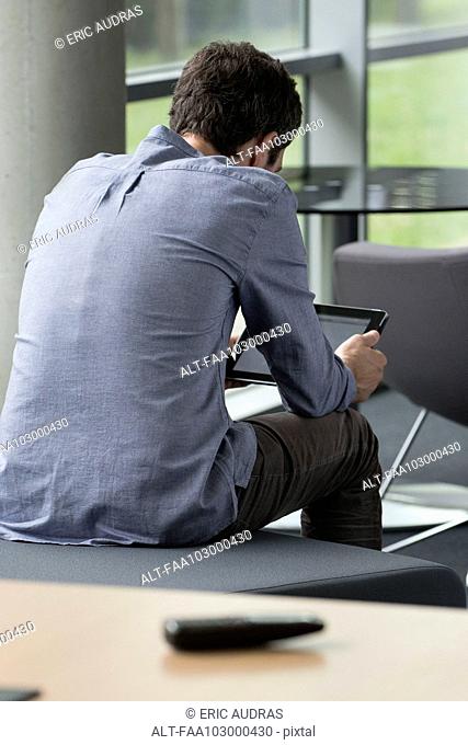 Man using digital tablet alone at home, rear view