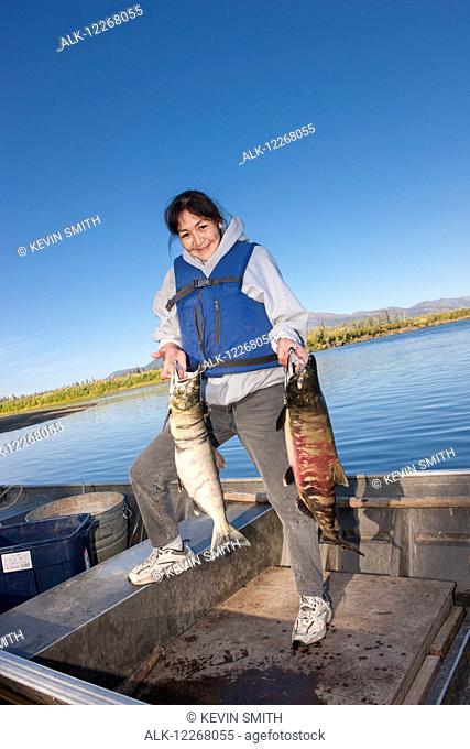 Alaska native female standing in a motor boat holding chum salmon, Shungnak, Arctic Alaska, summer