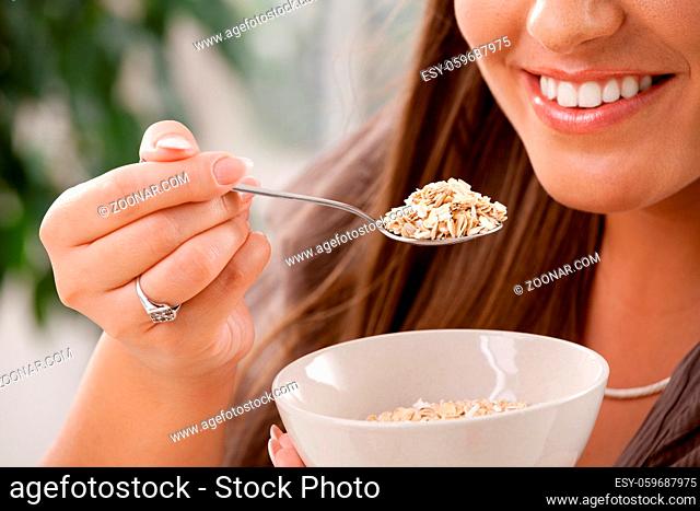 Closeup of partially visible young woman eating breakfast cereal. Selective focus on spoon