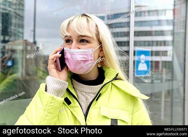 Close-up of young woman wearing face mask talking over mobile phone in city