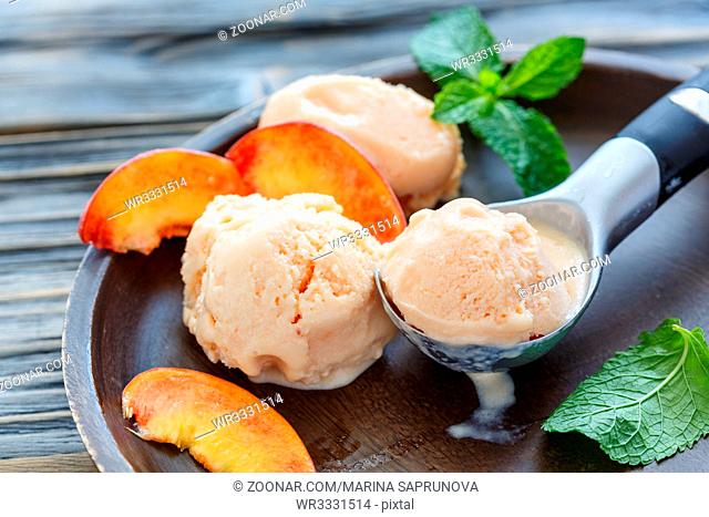 Homemade peach ice cream in a spoon, slices of peach and mint leaves on wooden plate, selective focus