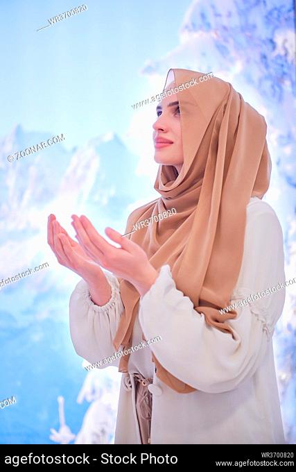 portrait of beautiful muslim woman in fashionable dress with hijab making traditional prayer to God, keeps hands in praying gesture isolated on modern winter...