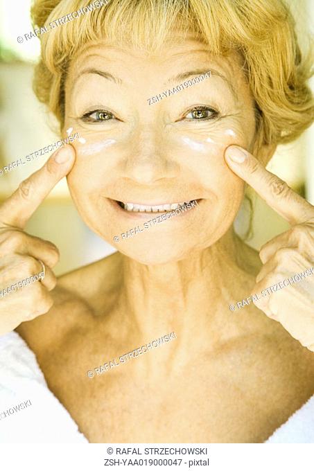 Senior woman applying moisturizer under eyes
