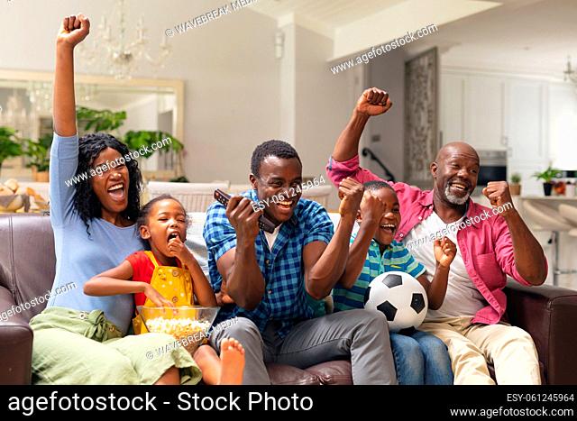 African american multi-generational family cheering while watching soccer match on tv at home