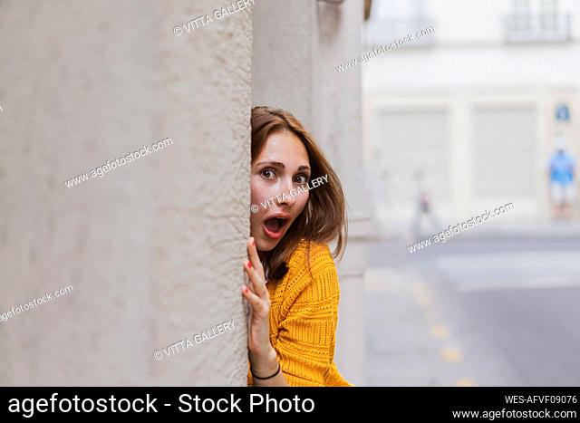 Surprised woman with brown hair peeking from wall