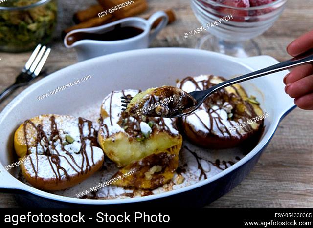 Caramelized apples with honey and cinnamon in a clay bowl pours chocolate hand takes a piece on a fork on a light wooden background. Top views