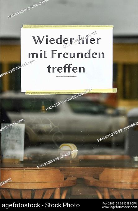 10 February 2021, Berlin: At the window of a bar in Friedrichshagen hangs a sign with the inscription ""Meet again here with friends""