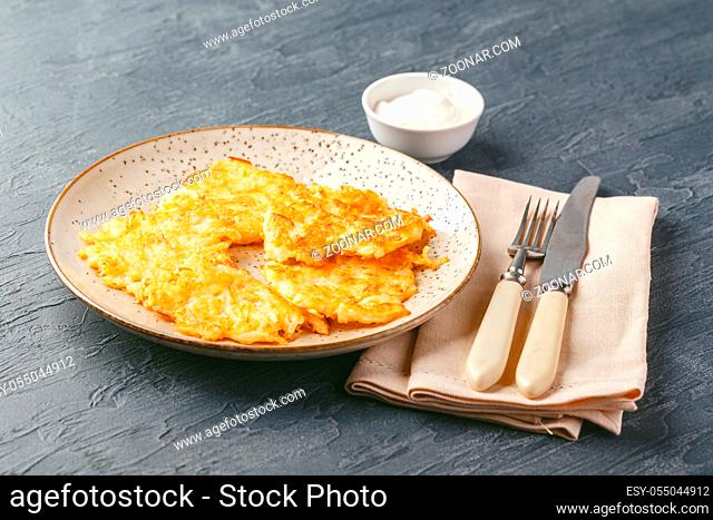 Hommade potato pancakes - rosti, hash browns, kartoffelpuffer, latkes, draniki - with sourcream on grey background