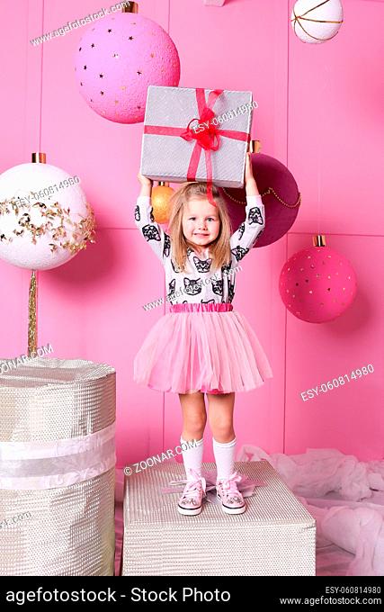 Pretty girl child 3 years old in a dress. Baby holding gift in their hands. Rose quartz room decorated holiday