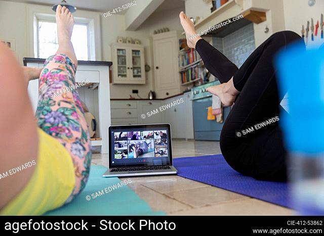 Women exercising online at laptop on kitchen floor