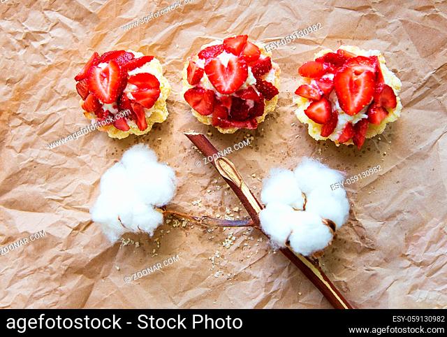 Beautiful cupcakes with strawberries along with a branch of cotton lies on kraft paper