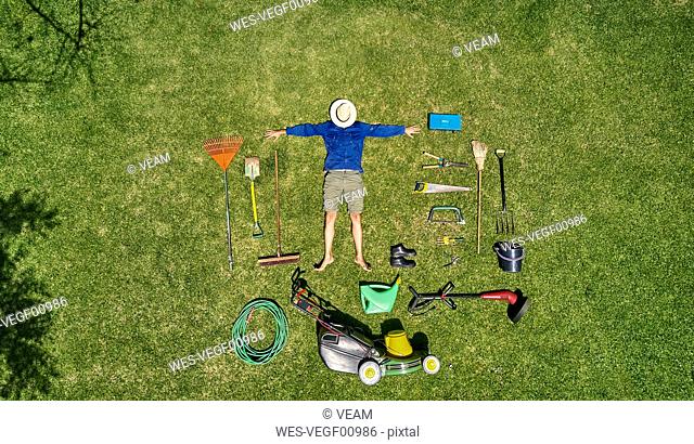 View from above of a gardener with sun hat on his face, laying on the grass with all the tools he need for take care of garden