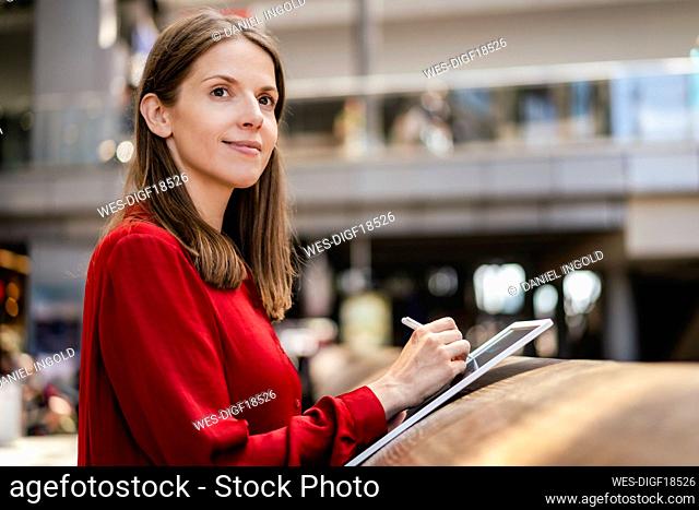Thoughtful businesswoman with digitized pen and tablet PC at workplace