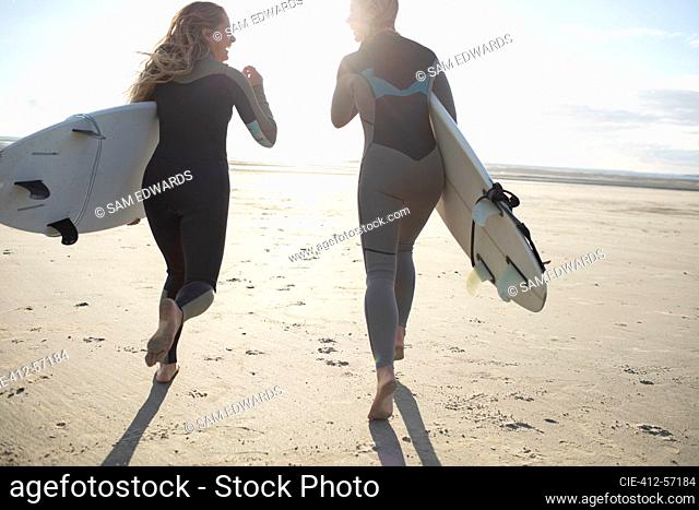 Carefree young female surfers running on sunny beach with surfboards