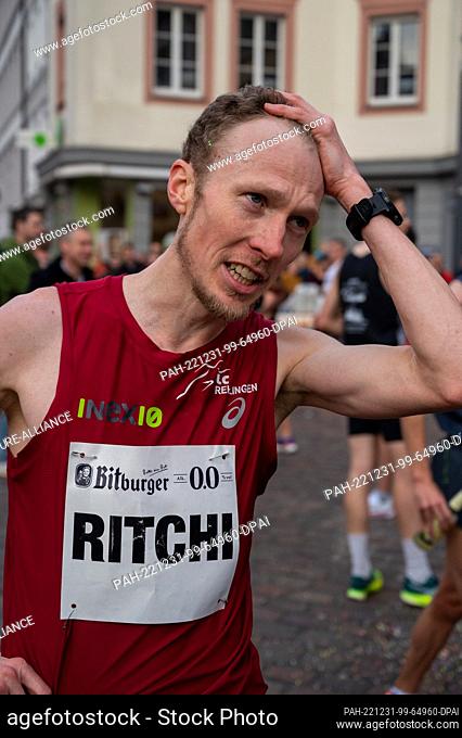 31 December 2022, Rhineland-Palatinate, Trier: Richard Ringer (LC Rehlingen) holds his hand to his head after his finish (2nd place) at the New Year's Eve run...