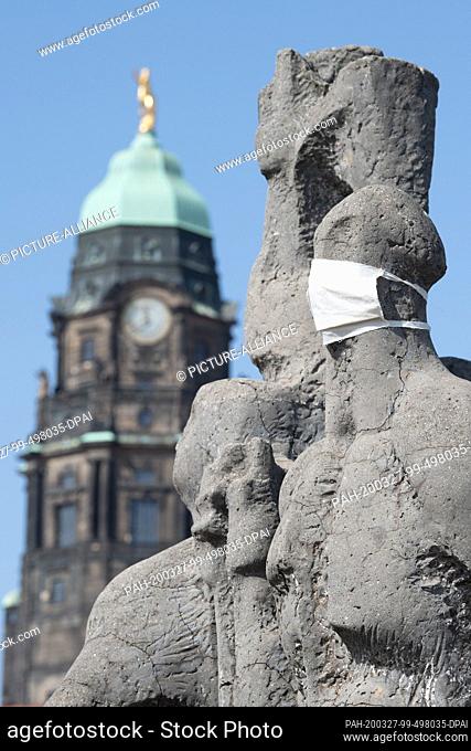 27 March 2020, Saxony, Dresden: Two face masks are pulled over the figures of the concrete sculpture ""Proletarian Internationalism"" by Vinzenz Wanitschke in...