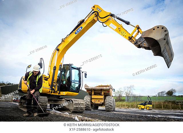 Yellow heavy JCB digger plant machinery at work on preparing and leveling the ground on a building site construction site UK