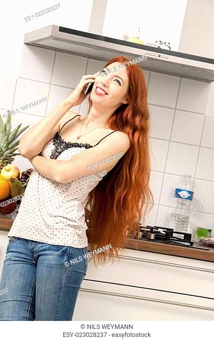 Glückliche junge Frau mit Handy Smartphone zu Hause in der Küche beim telefonieren