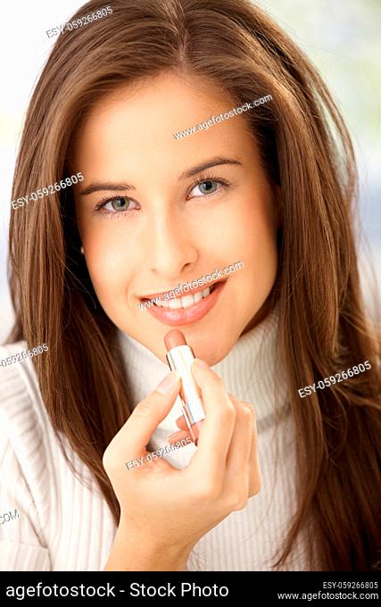 Portrait of happy woman applying lipstick, smiling at camera