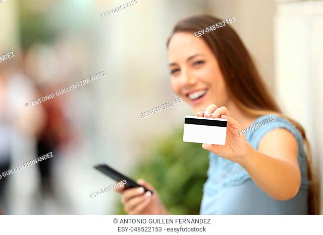 Happy on line buyer showing a credit card to the camera on the street