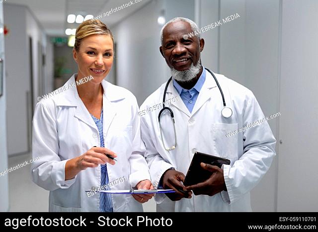 Portrait of diverse male and female doctors standing in hospital corridor smiling to camera