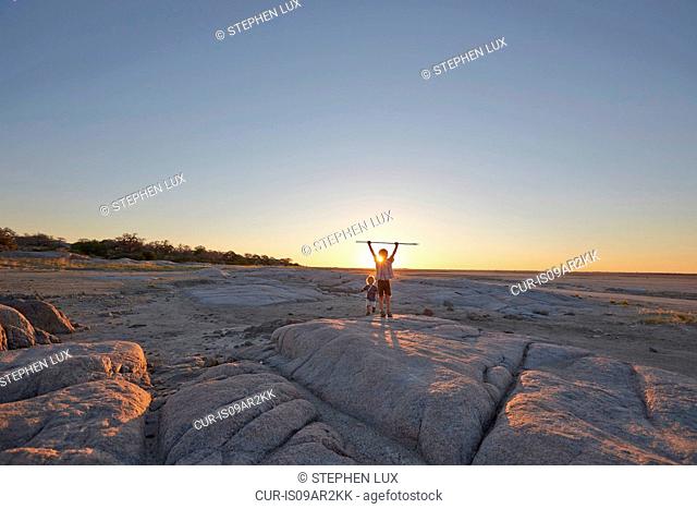Two boys standing on rock, holding spear in air, sunset, Gweta, makgadikgadi, Botswana