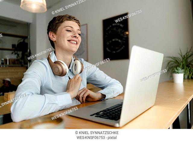 Happy businesswoman with laptop and headphones in a cafe