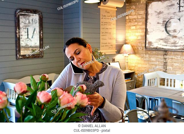 Mature female customer reading menu whilst talking on smartphone in cafe