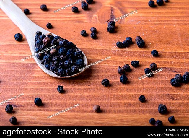 black color peppercorn seeds on wooden table with spoon
