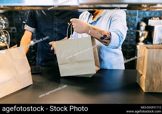 Midsection of chefs working together while holding paper bags at restaurant kitchen counter