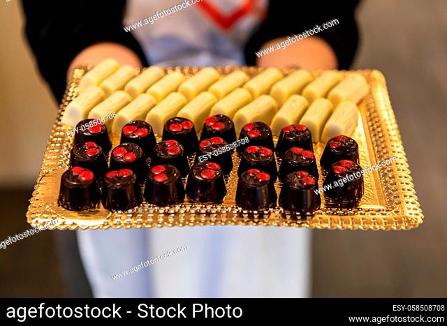 Selective focus on two types of delicious chocolate desserts on golden tray held by woman in blurred background. reception buffet candies and bonbons