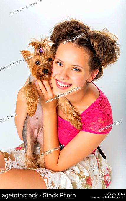 Beautiful young teenage girl in top and skirt holding small cute yorkshire terrier dog. Copy space. Studio shot on light background