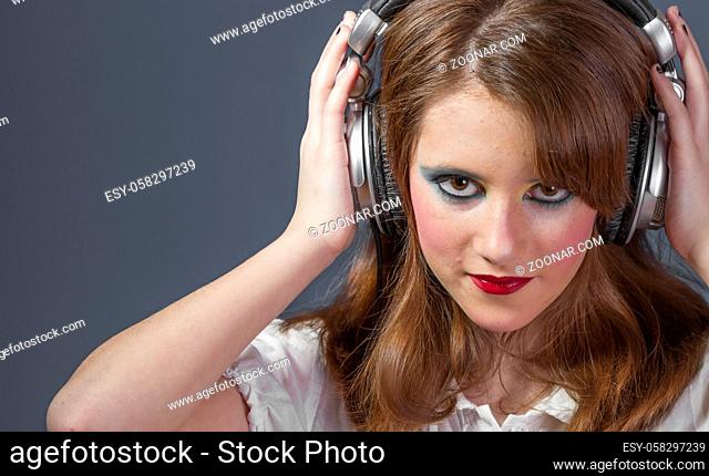 redhead girl with helmet on her head listening to music on a flat gray background
