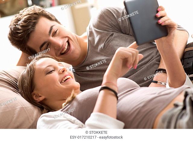 Happy young couple lying on the bed in a bedroom and using digital tablet