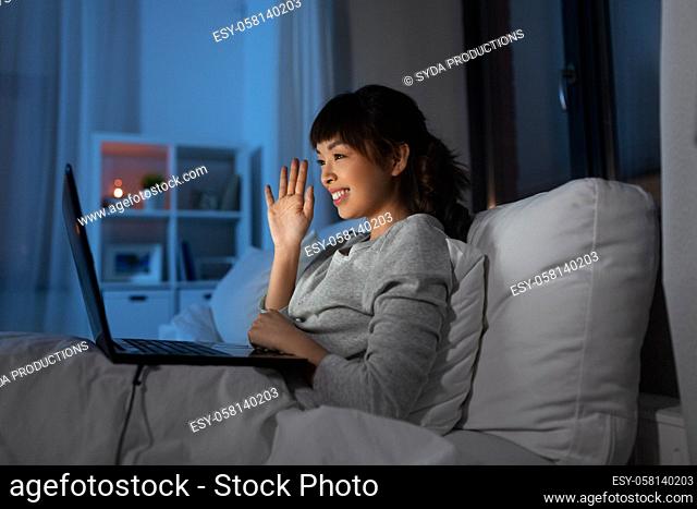 woman having video call on laptop in bed at night