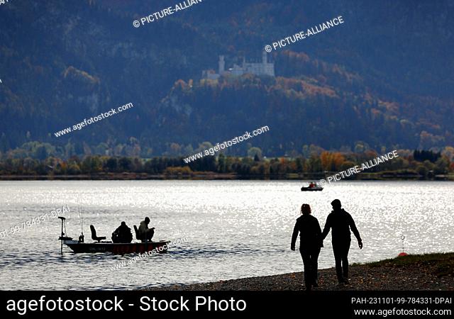 01 November 2023, Bavaria, Roßhaupten: Excursionists enjoy the sunny weather on the shore of Lake Forggensee, located below Neuschwanstein Castle