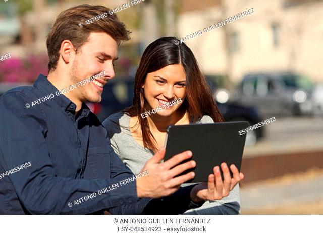 Happy couple watching media content in a tablet sitting outdoors in a park