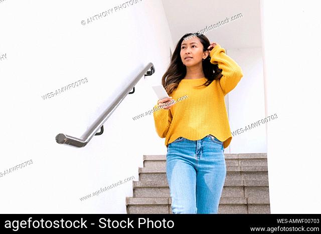 Thoughtful young woman with mobile phone moving down on steps