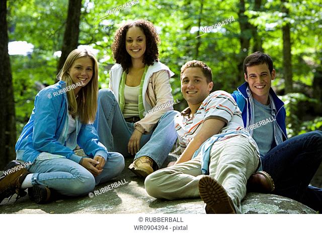 Portrait of two young women and two young men sitting on a rock and smiling