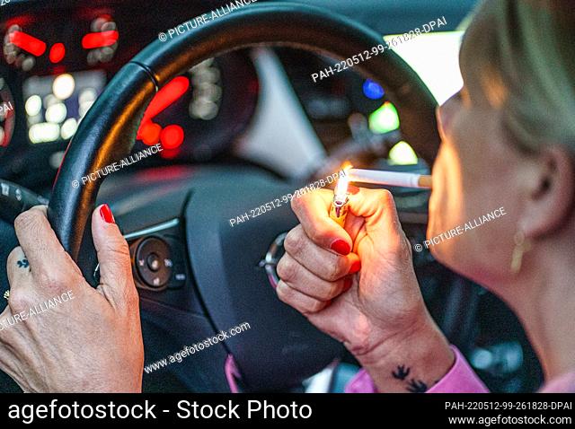 11 May 2022, Schleswig-Holstein, Flensburg: A woman lights a cigarette behind the wheel of her car. Photo: Axel Heimken/dpa