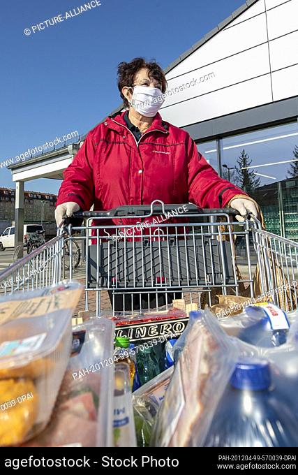 24 March 2020, Saxony, Heidenau: A woman wears a mouth-and-nose protector and disposable gloves and pushes the purchases to the car in a parking lot