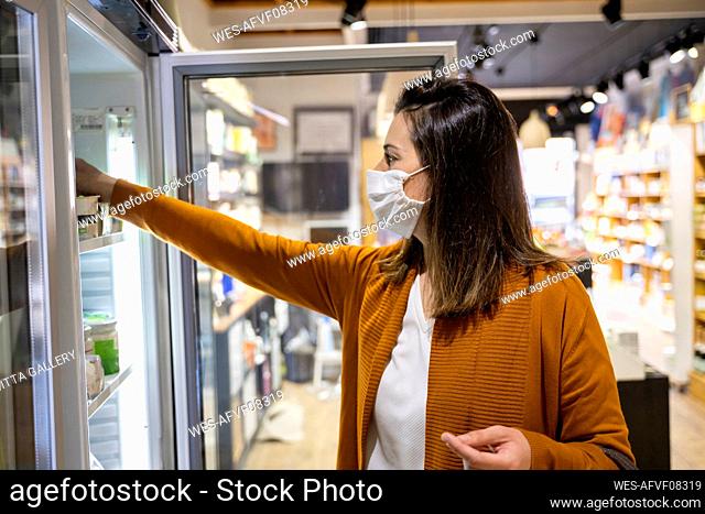 Young woman reaching for food in refrigerator at store