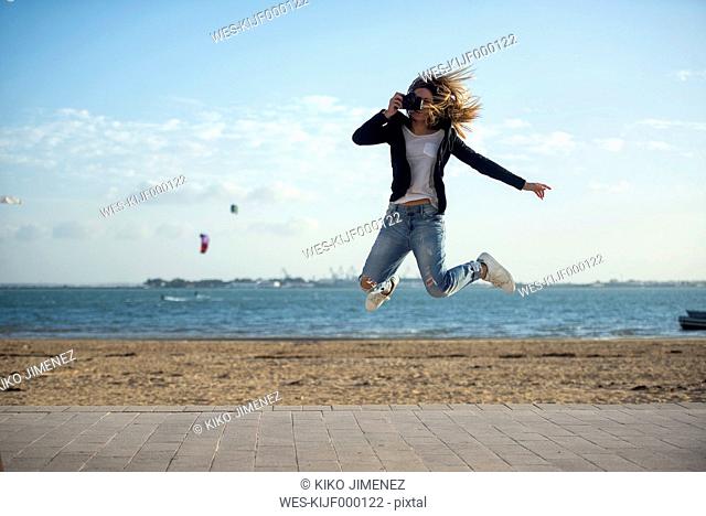 Spain, Puerto Real, woman taking a picture while jumping in the air