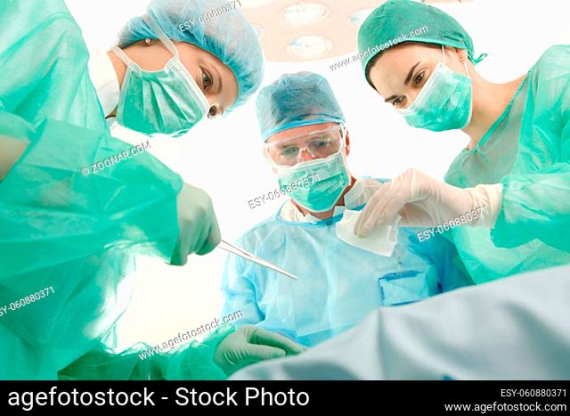 Surgeons and medical assistant wearing mask and uniform operating patient
