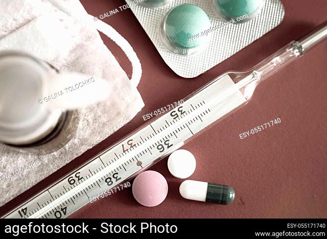 Medicines for the treatment of flu, colds on a red background: face mask, thermometer, pills, nose drops, syringe. Presented close-up