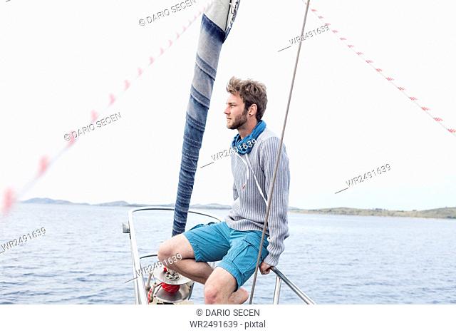 Young man sits on bow of yacht day dreaming