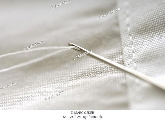 Needle and thread on white cloth (part of), close-up
