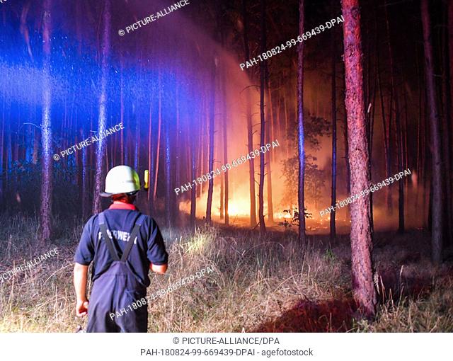 24.08.2018, Brandenburg, Klausdorf: Brightly lit is a burning forest near Klausdorf, which is currently being tried to extinguish with a jet of water from a...