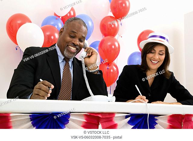 USA, Illinois, Metamora, Smiling man and woman at polling place table, red and blue balloons in background
