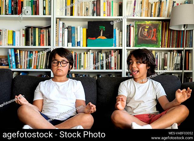 Boy sitting on couch meditating, his brother teasing him